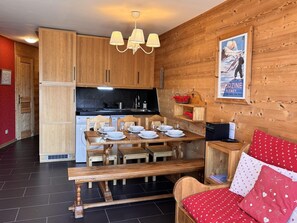 A cozy cabin-style room with wooden walls, a dining table set with plates and glasses, a bench, and a bed with red bedding.