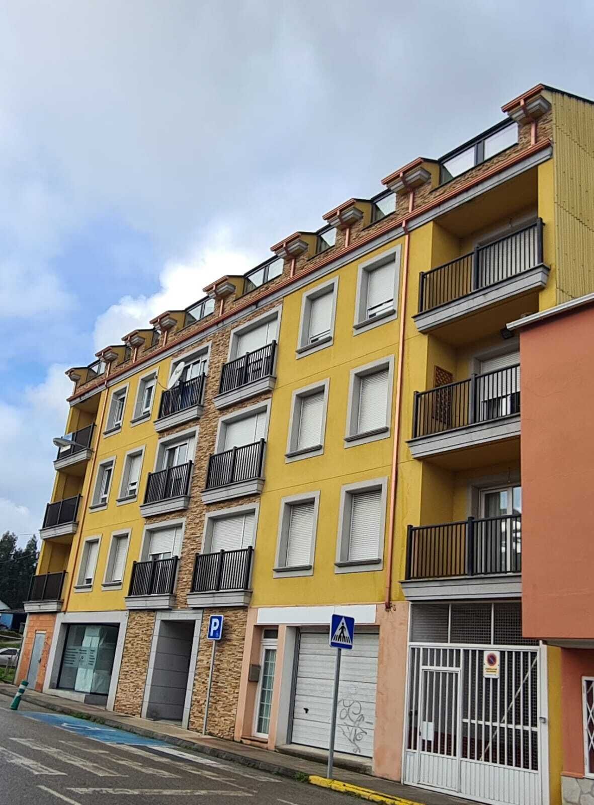 Un edifici residencial de diverses plantes amb balcons, zona d'aparcament i entrada tancada per reixa.