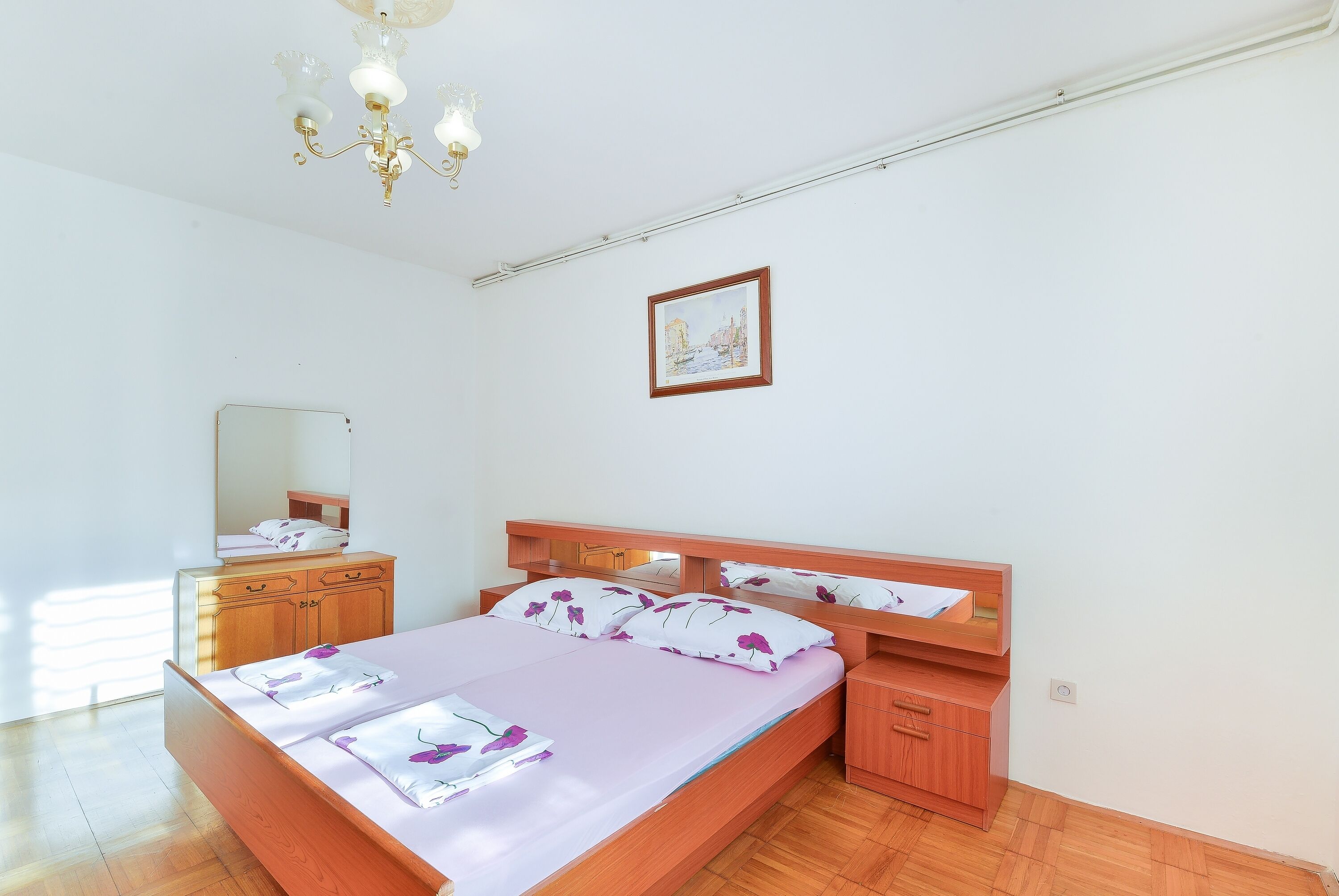 A bedroom with a wooden bed, a nightstand, a dresser, a mirror, and a chandelier.