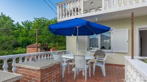A balcony with a table and chairs, a blue umbrella, and a brick wall. - Apartment Basic Mario (Vir)