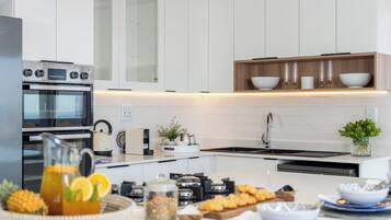 A modern kitchen with white cabinets, a built-in oven, a sink, and a countertop with various items including a pitcher, a bowl, and a basket of food.