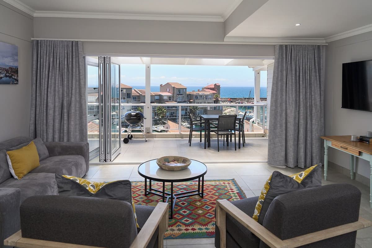 A modern living room with a balcony, grey sofas, a coffee table, and a TV.