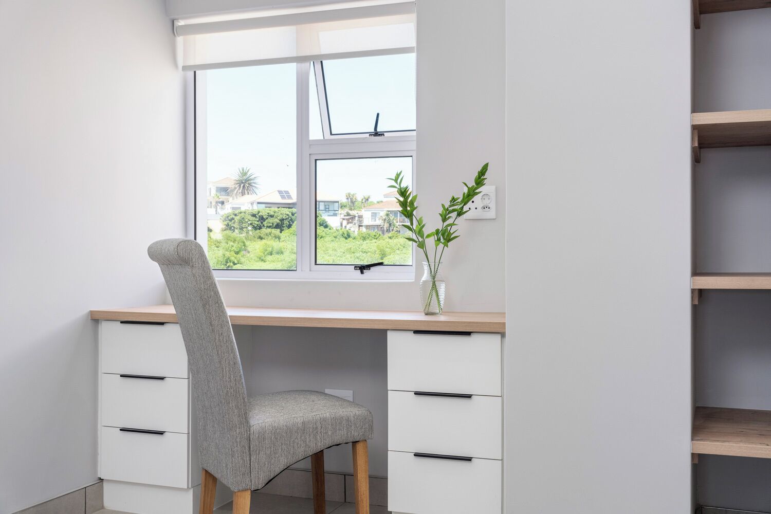A study with a desk, chair, and a window with a view of greenery and buildings.