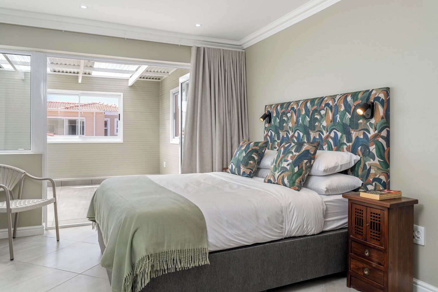Une chambre à coucher avec un lit, une chaise, une table de chevet et une vue sur l’extérieur.