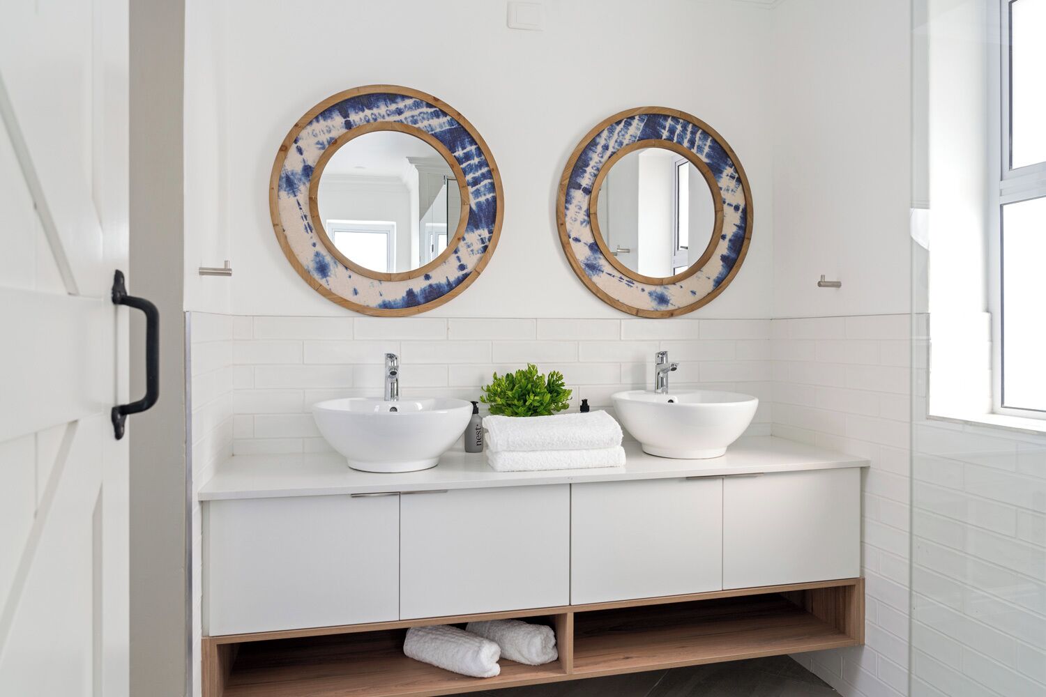 A bathroom with two white sinks, a mirror, and a small plant on the vanity.