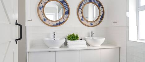 A bathroom with two white sinks, a mirror, and a small plant on the vanity.