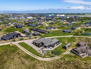 Vista aérea de uma área residencial com casas, um edifício grande com piscina e uma construção com telhado de palha.