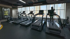 A gym with treadmills, stationary bikes, and a large window with a city view.