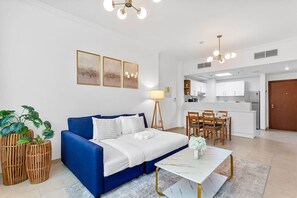 A modern living room with a blue sofa, a dining table, and a kitchen area in the background.