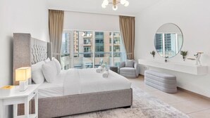 A modern bedroom with a large bed, a sitting area, and a view of the city through large windows.