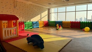 A playroom with colorful play structures, a soft play mat, and a large window with a city view. - Cobalt refurbished 1 Bedroom  in Downtown Dubai (Dubai)