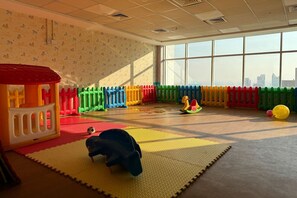 Ein Spielzimmer mit bunten Spielgeräten, einer weichen Krabbeldecke und einem großen Fenster mit Blick auf die Stadt.