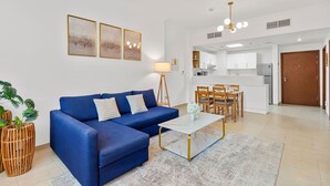 A modern living room with a blue sofa, a white coffee table, and a dining area with wooden chairs and a white table.