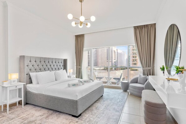 A modern hotel room with a large bed, a desk, a chair, and a balcony with a view of the city.