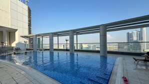 A rooftop swimming pool with clear blue water, surrounded by a modern architectural structure with large windows offering views of the city skyline. - Cobalt refurbished 1 Bedroom  in Downtown Dubai (Dubai)