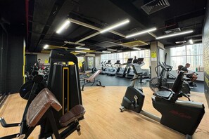 Et fitnessrum med løbebånd, styrketræningsudstyr og trægulv.