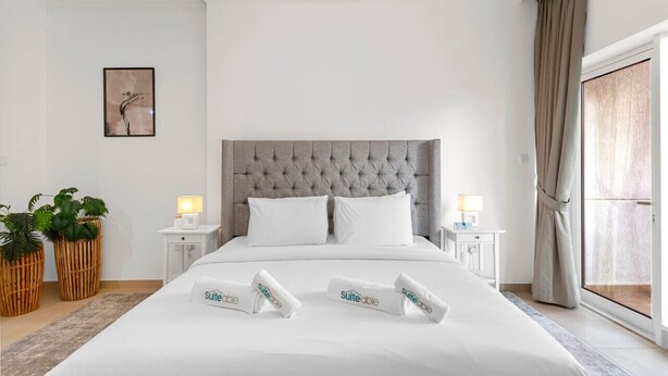A hotel room with a large bed, two bedside tables with lamps, a grey tufted headboard, and a large window with curtains. - Cobalt refurbished 1 Bedroom  in Downtown Dubai (Dubai)