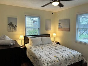 A bedroom with a bed, two bedside lamps, a ceiling fan, and artwork on the walls.