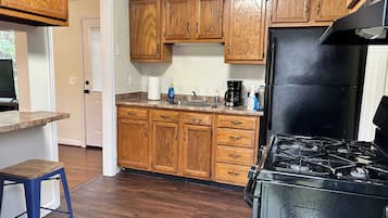 Una cucina con mobili in legno, un frigorifero nero, un piano cottura a gas e uno sgabello blu.