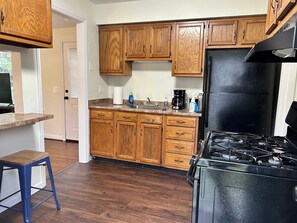 A kitchen with wooden cabinets, a black refrigerator, a gas stove, and a blue stool.