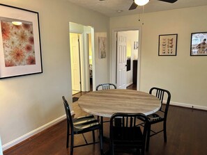A dining area with a round wooden table, four black chairs, and framed floral artwork on the walls.