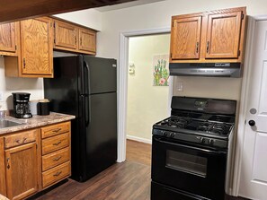 A kitchen with wooden cabinets, a black refrigerator, a stove, and a coffee maker.