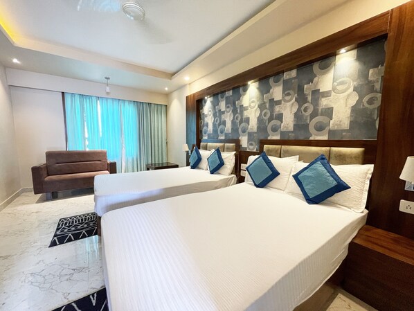Habitación de hotel con dos camas, un sofá, un escritorio y un papel tapiz estampado.