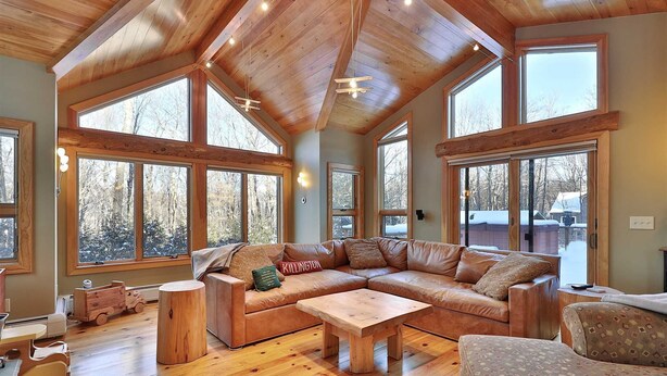 Amplia sala de estar con un sofá seccional grande, piso de madera y amplias ventanas que ofrecen vistas al exterior.
