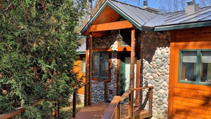 Una cabaña con fachada de piedra, terraza de madera y una escalera de piedra que lleva a la entrada.