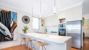 Una cocina moderna con una isla central, taburetes de bar, un refrigerador y un ventanal grande.