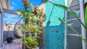 Un pequeño espacio al aire libre con un muro de azulejos, una silla colgante y varias macetas con plantas.