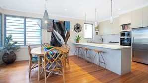 Una cocina moderna con una isla central, suelo de madera y un comedor con sillas de mimbre.