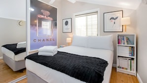 Une chambre d’hôtel avec un grand lit, une table de chevet avec une lampe, une bibliothèque et un miroir qui reflète la pièce.
