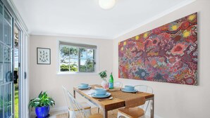 Un coin repas avec une table dressée pour quatre personnes, une grande peinture abstraite au mur et une vue sur la verdure à l’extérieur.