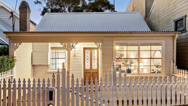 Une petite maison à un étage, avec une clôture blanche en bois, un porche à l’avant et un garage.