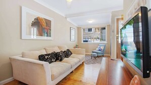 Un salon avec un canapé beige, une table basse en bois, un téléviseur à écran plat et un ventilateur de plafond.