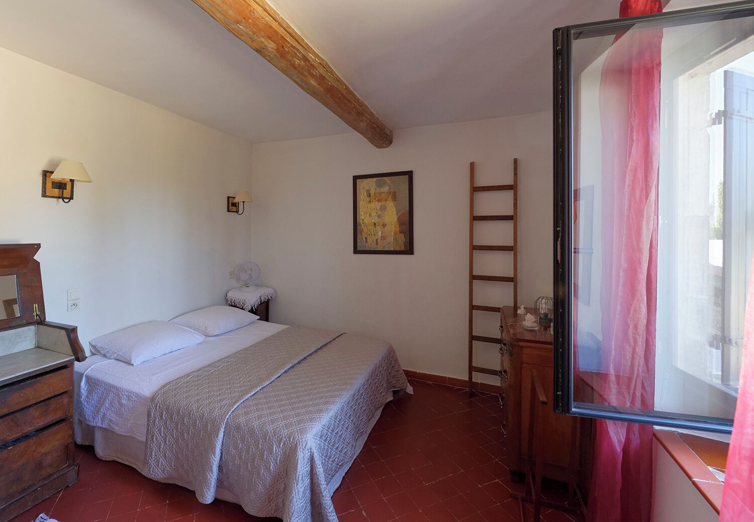 A bedroom with a bed, a wooden dresser, a ladder, and a painting on the wall.