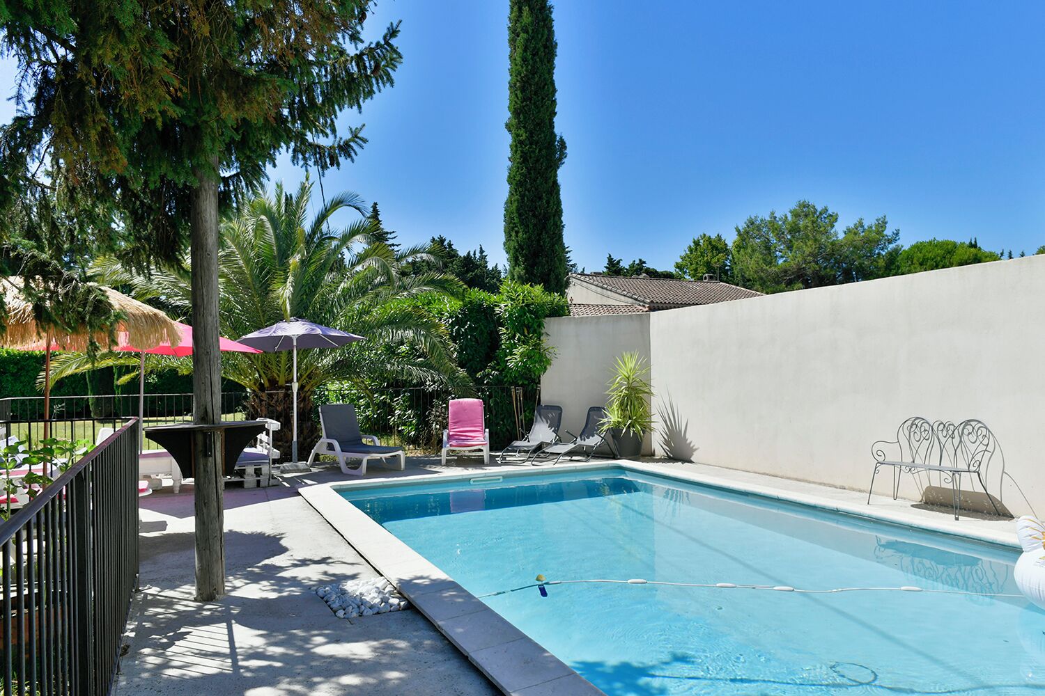 A swimming pool with lounge chairs and umbrellas, surrounded by greenery and a white wall.
