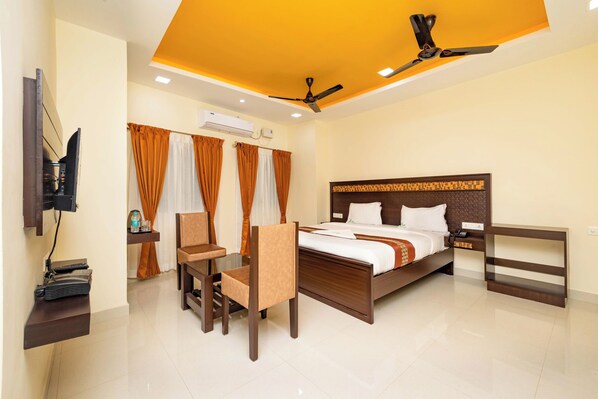 A hotel room with a bed, a desk with a chair, a television, and an air conditioning unit.