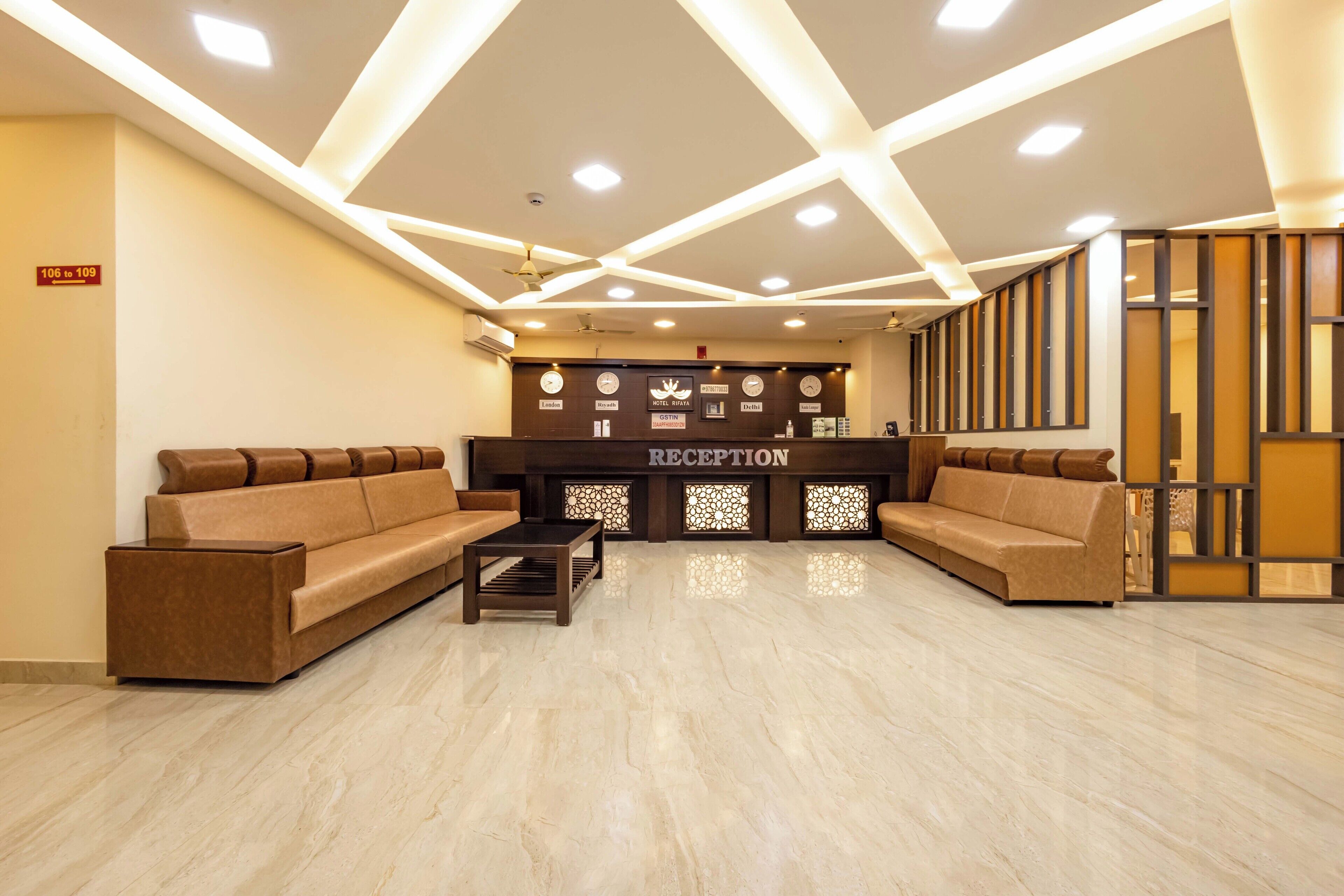 Un área de recepción con una mesa de recepción, dos sofás, una mesa de centro y una pared decorativa con un letrero que dice “RECEPTION”.