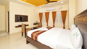 A hotel room with a bed, a desk, a chair, a television, and an air conditioning unit.