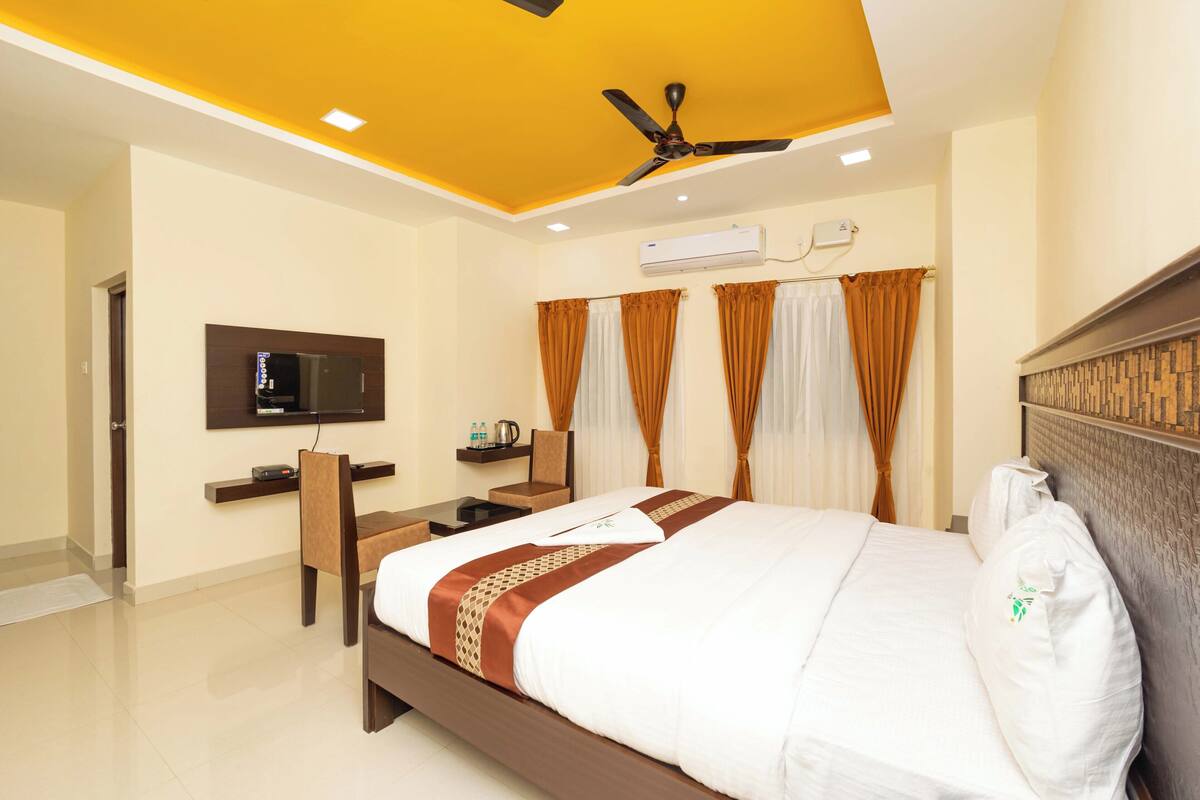 Una habitación de hotel con cama, escritorio, silla, televisor y aire acondicionado.