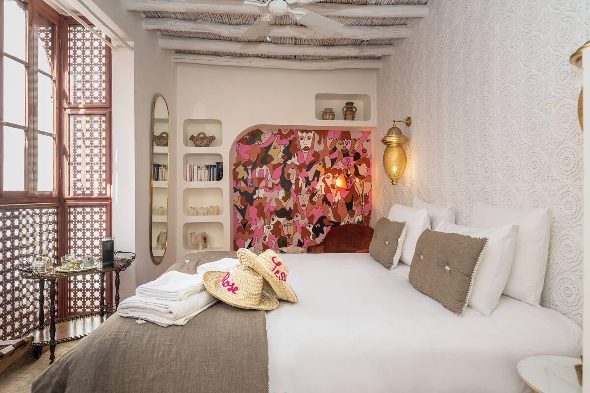 A bedroom with a large bed, a nightstand, a bookshelf, and a decorative wall mural.
