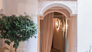 A hallway with a decorative archway, potted plants, and a staircase leading to a room. - Le Singe Rose (Marrakech)
