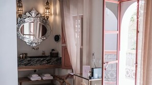 A bedroom with a bed, a vanity with a mirror, a wooden ceiling, and a view of the outside. - Le Singe Rose (Marrakech)