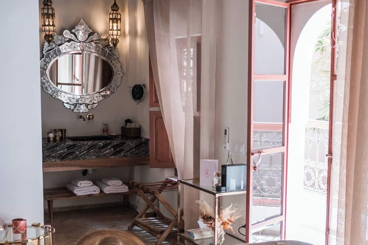 A bedroom with a bed, a vanity with a mirror, a wooden ceiling, and a view of the outside.