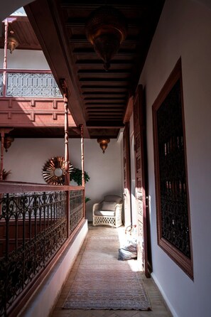 Un pasillo con barandilla de madera, alfombra estampada y una silla.