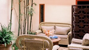 A cozy indoor seating area with wicker furniture, a bamboo plant, and a wooden partition. - Le Singe Rose (Marrakech)