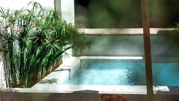 A poolside area with lounge chairs and hats, a tiled pool, and lush greenery. - Le Singe Rose (Marrakech)