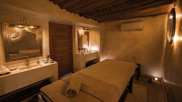 Una habitación con una cama, una puerta de madera, un espejo, un lavabo y una toalla sobre la cama.